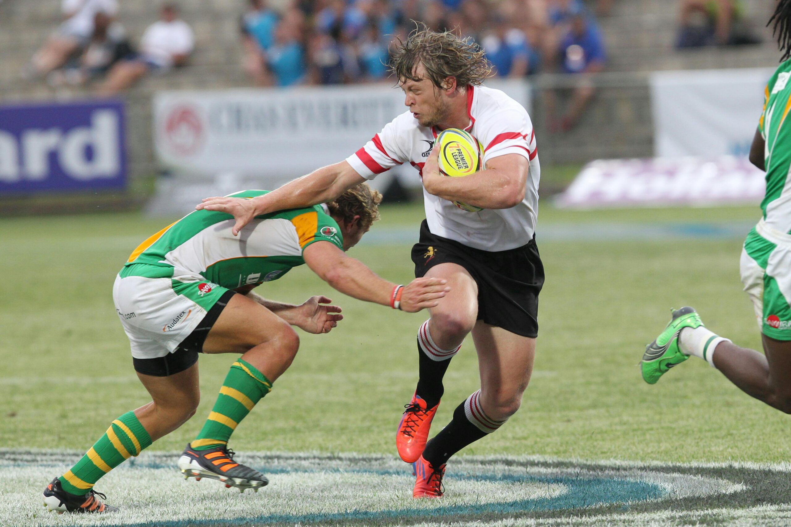 Dynamic action shot of rugby players in an intense tackle during a competitive match on a grass field.