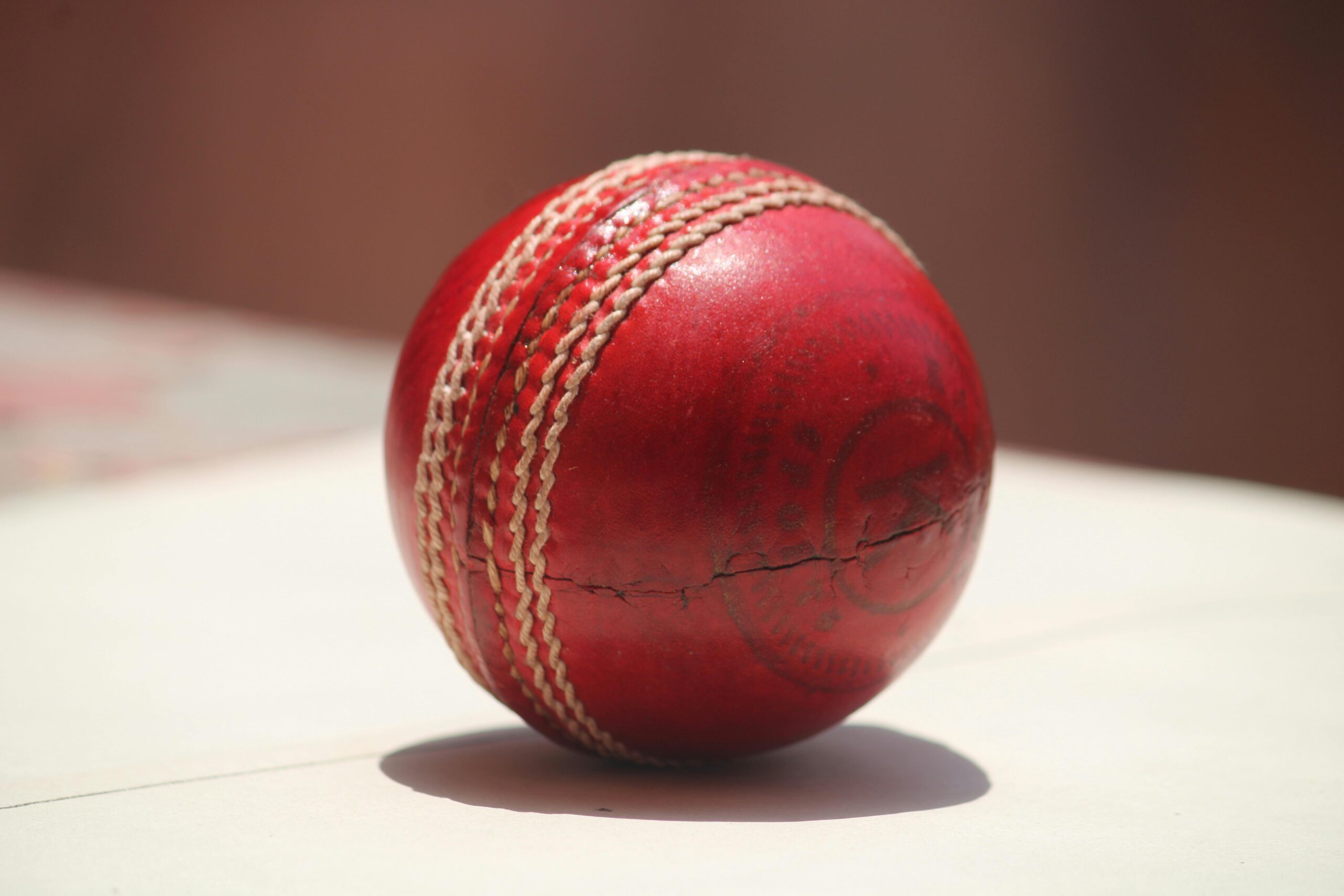 Detailed close-up of a red leather cricket ball showing wear and stitching.